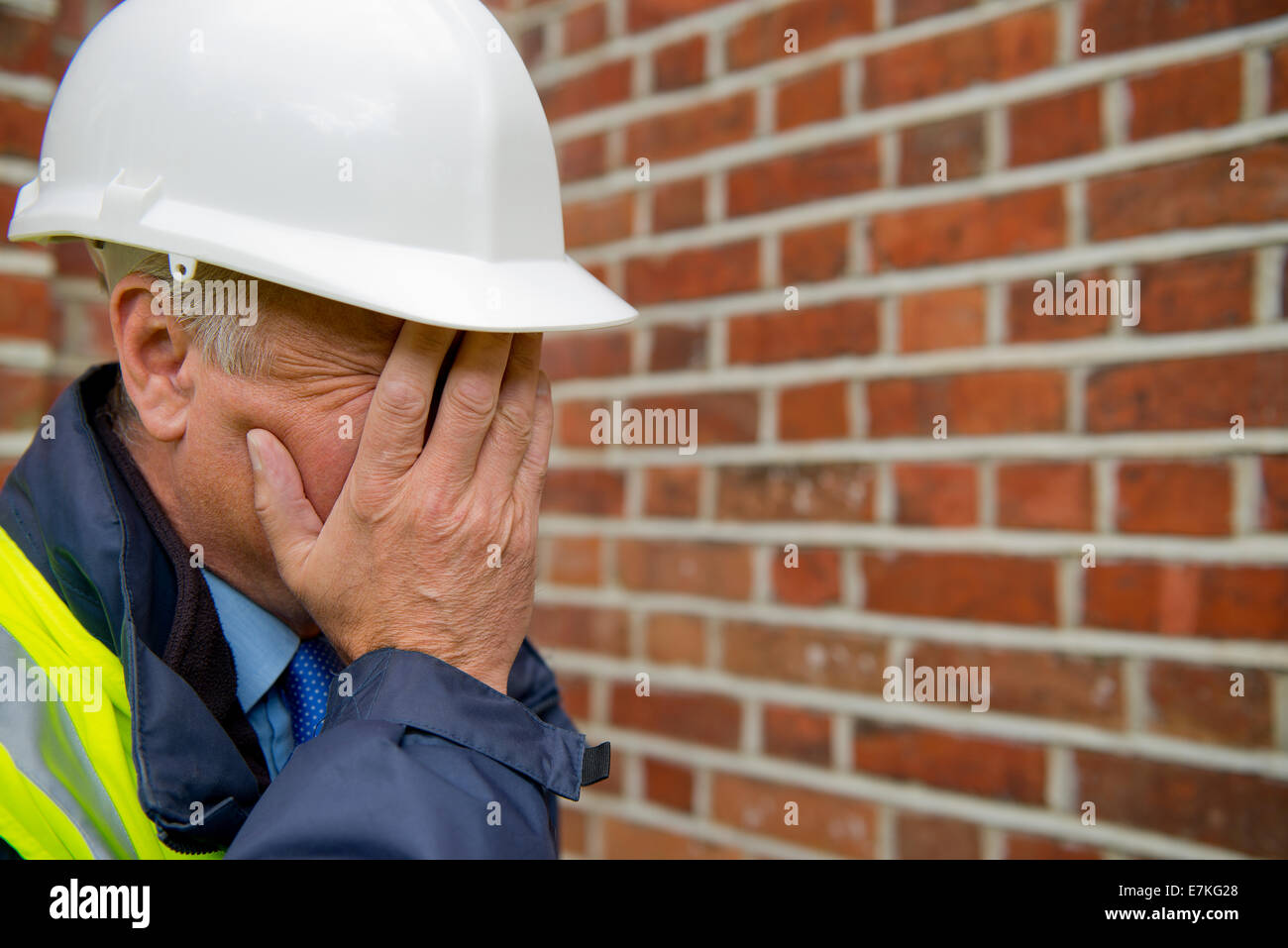 Sconvolto imprenditore edile, con le mani che coprono il suo volto, e indossando un bianco casco di sicurezza. Foto Stock