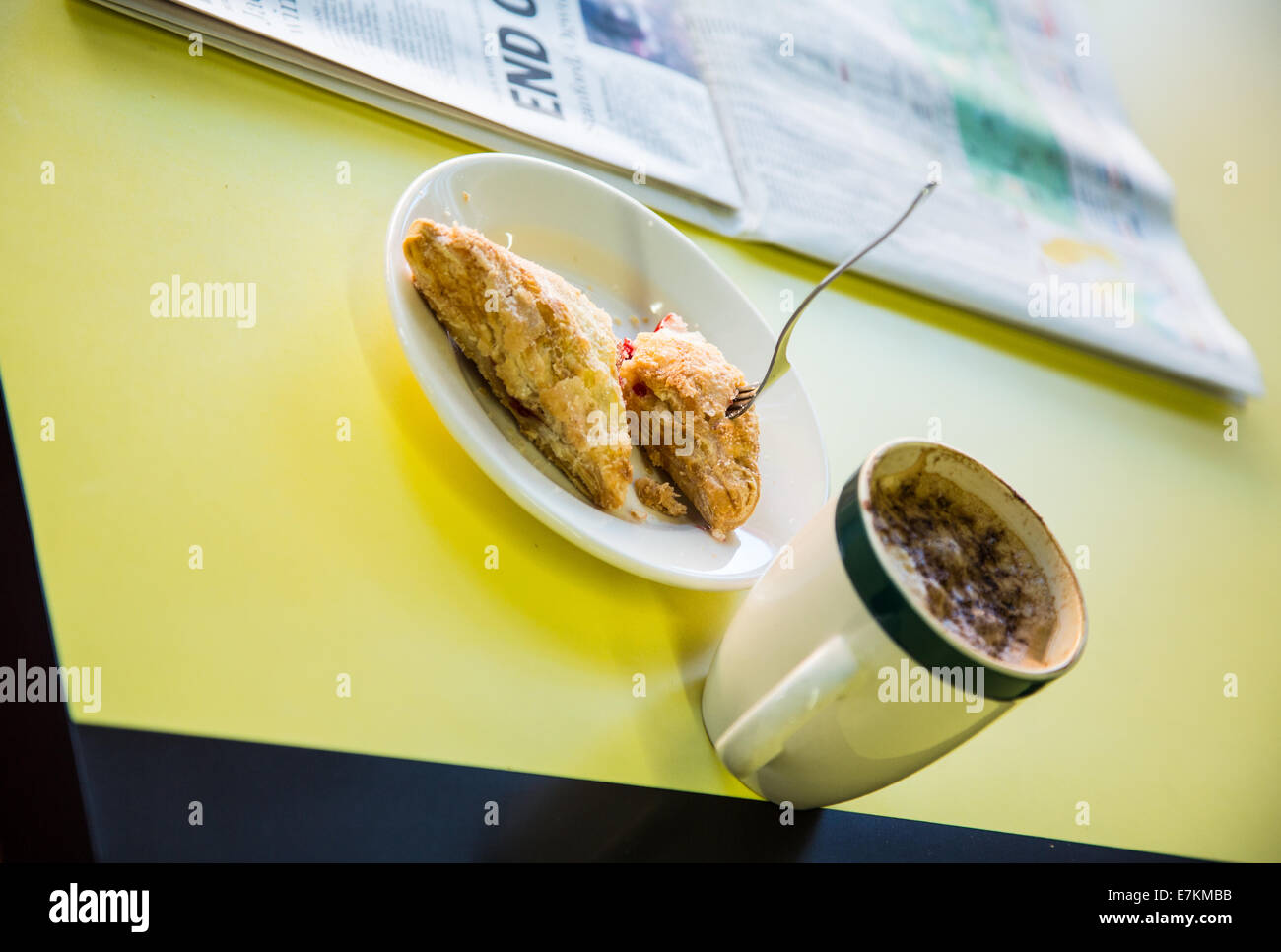 Una forcella sorge in una pasticceria uneaten con una tazza di caffè e un giornale. Foto Stock