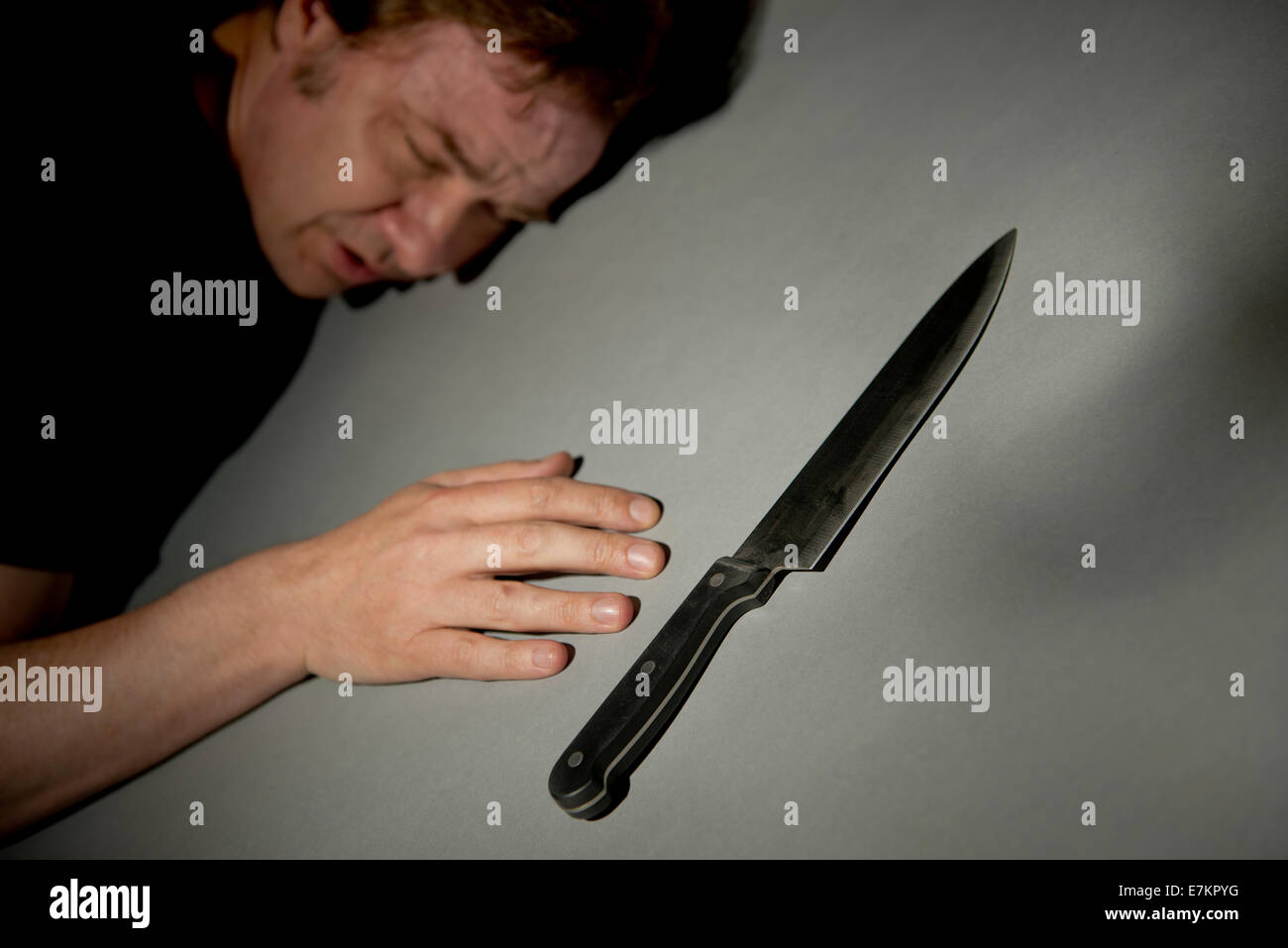Angolo di visualizzazione di un uomo sdraiato a faccia in giù sul pavimento con un letale coltello da cucina in primo piano. Foto Stock