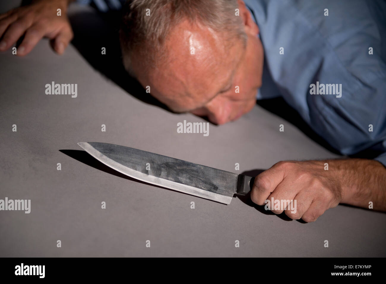 Angolo di visualizzazione di un uomo sdraiato a faccia in giù sul pavimento, tenendo una letale coltello da cucina. Foto Stock