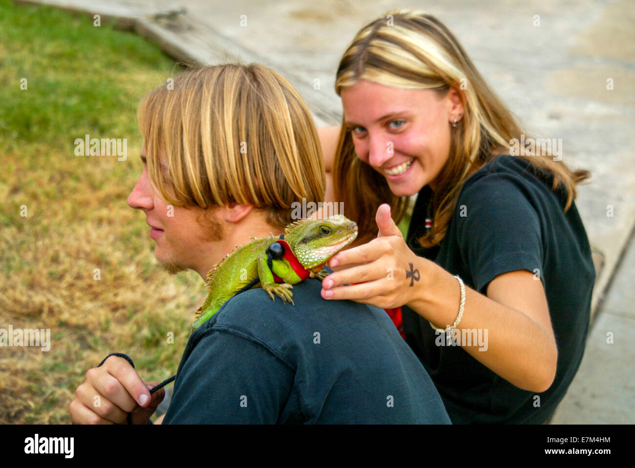 Un divertito teen ragazza ragazza solletica il suo fidanzato la pet iguana in un concerto all'aperto nella valle del Cedro, CA. Nota mancanza di paura. Foto Stock