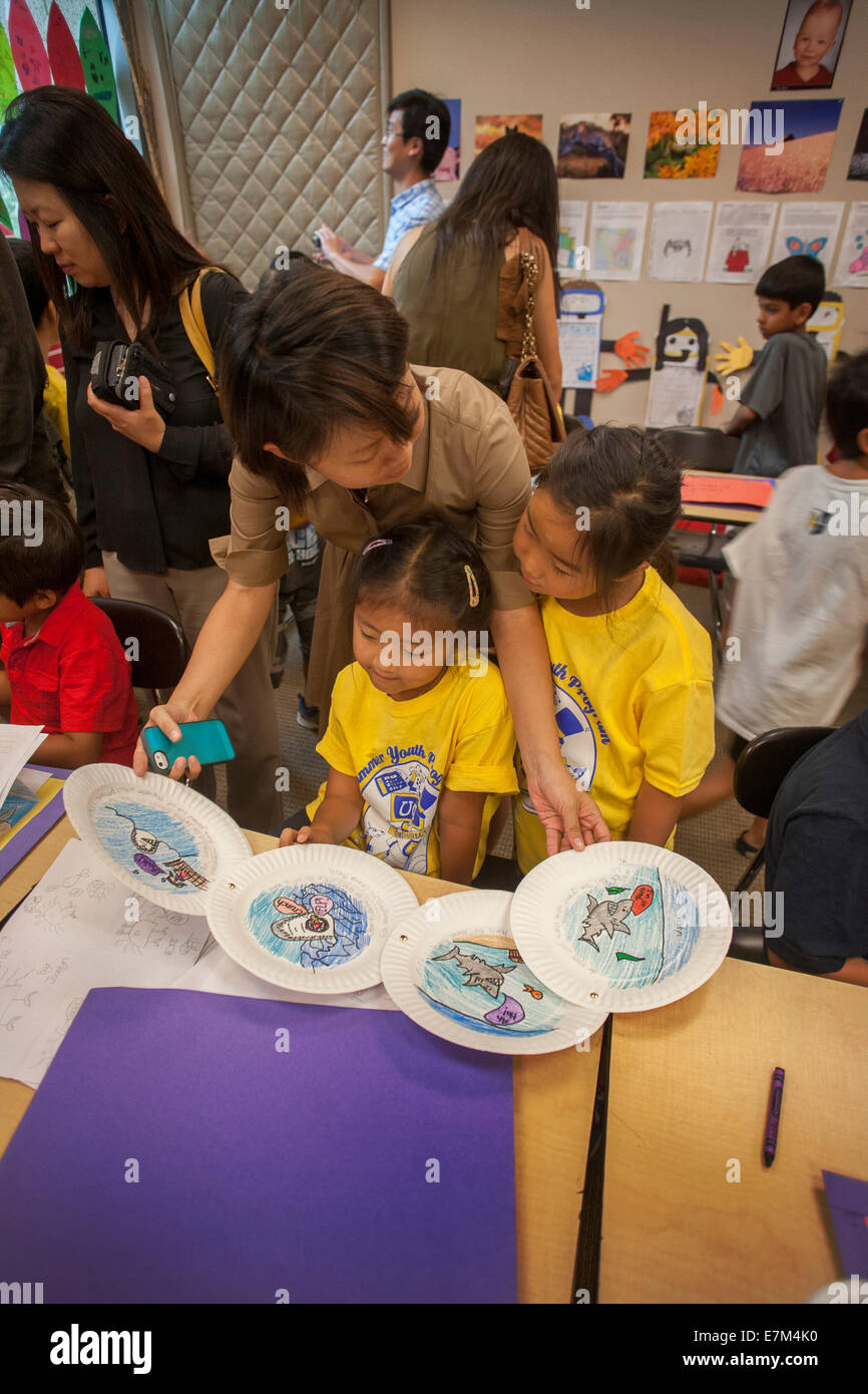 Un americano asiatico insegnante mostra due dei suoi studenti esempi di illustrazione su piastre di carta a un Irvine, CA, scuola elementare come parte di un estate programma di apprendimento. Nota giallo T shirt. Foto Stock