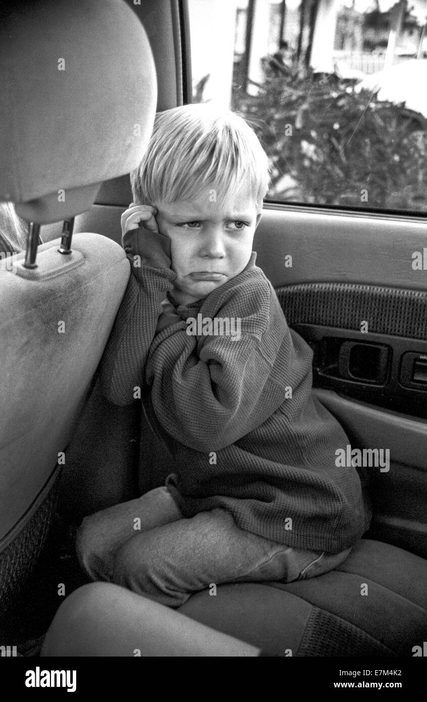 Un ragazzo arrabbiato fa il broncio sul sedile posteriore di un auto in Corona, CA. Nota il linguaggio del corpo. Foto Stock