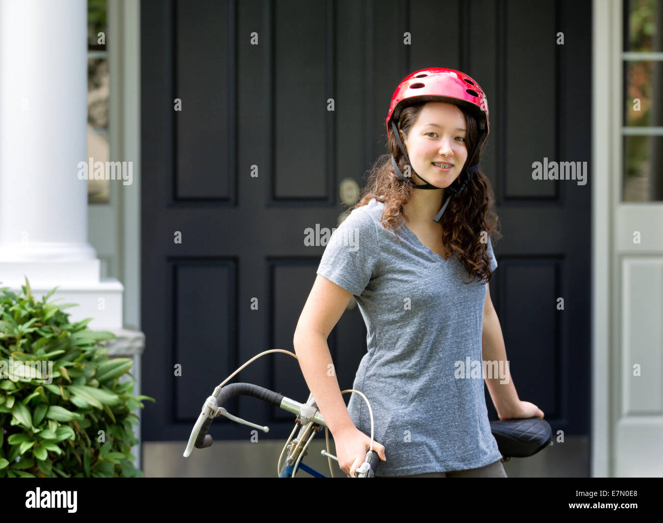 Immagine della ragazza adolescente, guardando avanti con il casco in testa, mentre in appoggio contro la sua bicicletta con home in background Foto Stock