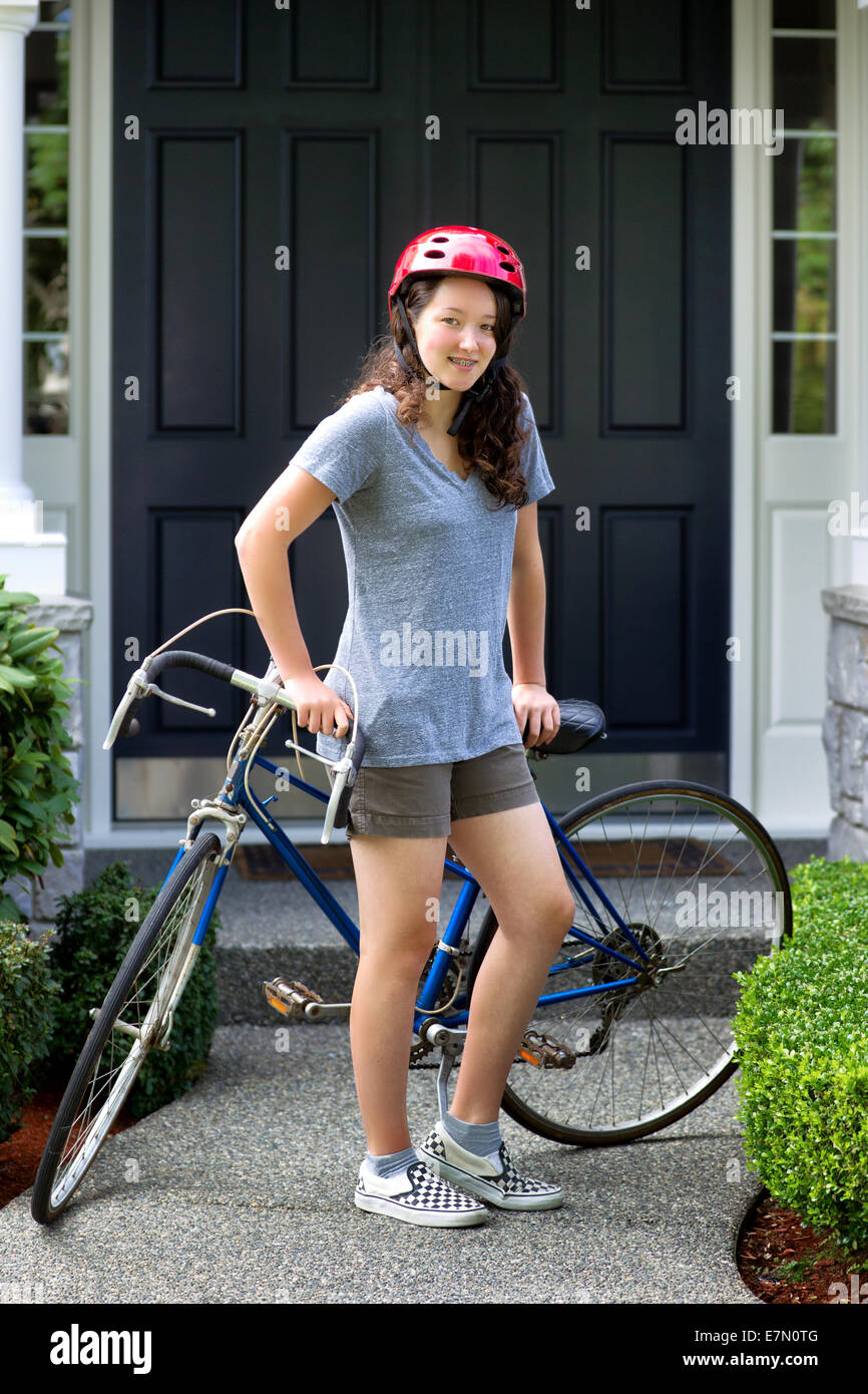 L'immagine verticale della ragazza adolescente, guardando avanti, mentre in appoggio contro la sua bicicletta con home in background Foto Stock