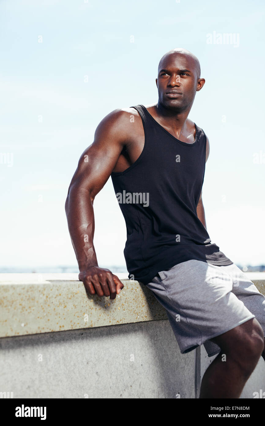 All'aperto colpo di sano giovane uomo seduto su una parete che guarda lontano sul serio. Africa muscolare modello maschile. Foto Stock