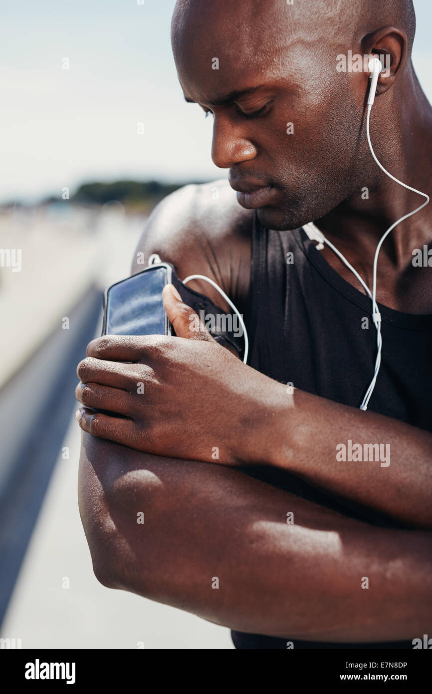 Africa atleta muscolare ascoltando musica. Modello maschile ascoltando la musica dal suo telefono cellulare sulla fascia da braccio. Foto Stock