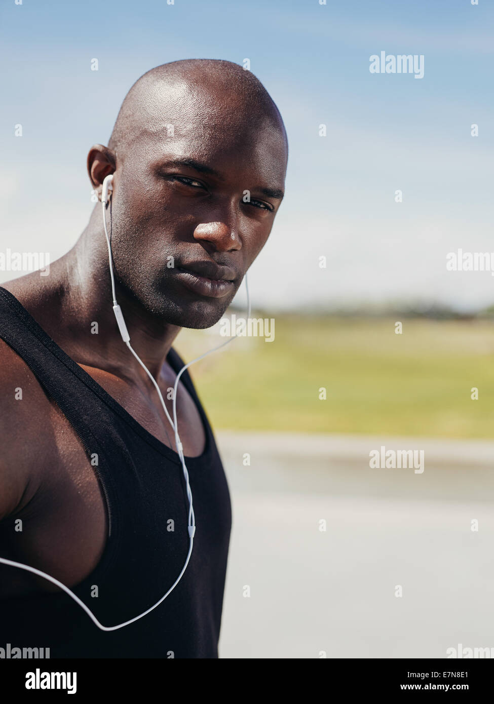 Immagine del bel giovane uomo che indossa gli auricolari guardando la fotocamera. African maschio modello all'esterno. Foto Stock