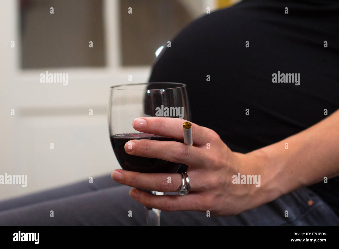 Donna incinta tenendo una sigaretta e bicchiere di vino Foto Stock