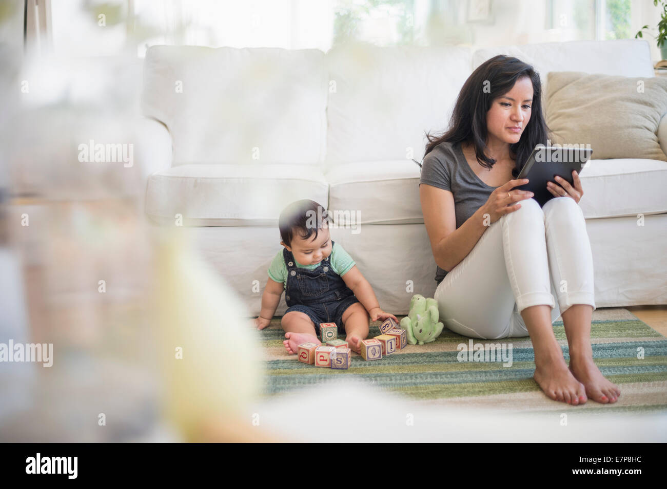 Madre utilizzando un tablet pc mentre suo figlio (6-11 mesi) giocando con i blocchi di costruzione Foto Stock