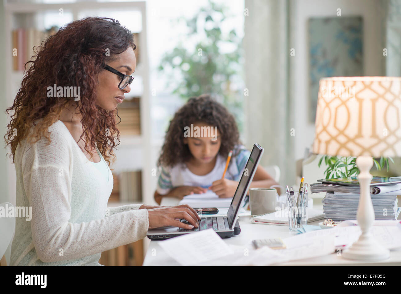Donna che utilizza portatile a casa, ragazza (8-9) facendo i compiti in background Foto Stock