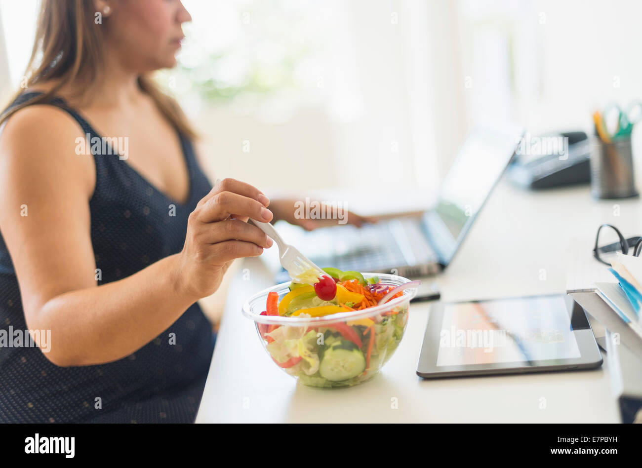 Donna che lavorano in ufficio a casa e mangiare insalata Foto Stock