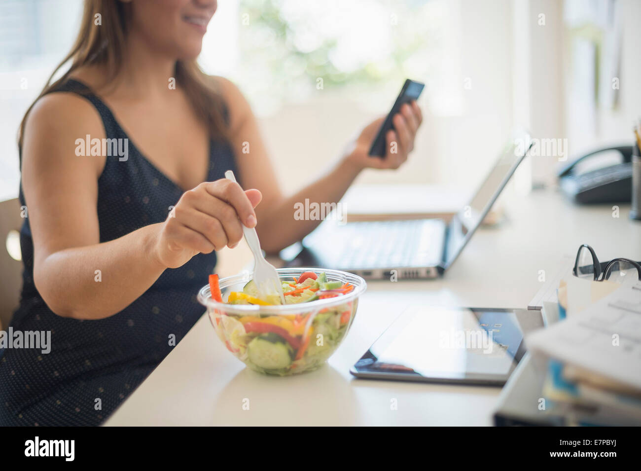 Donna che lavorano in ufficio a casa e mangiare insalata Foto Stock