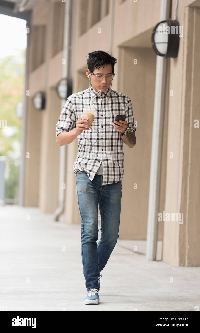 Uomo a camminare sul marciapiede con caffè ghiacciato e il telefono cellulare Foto Stock