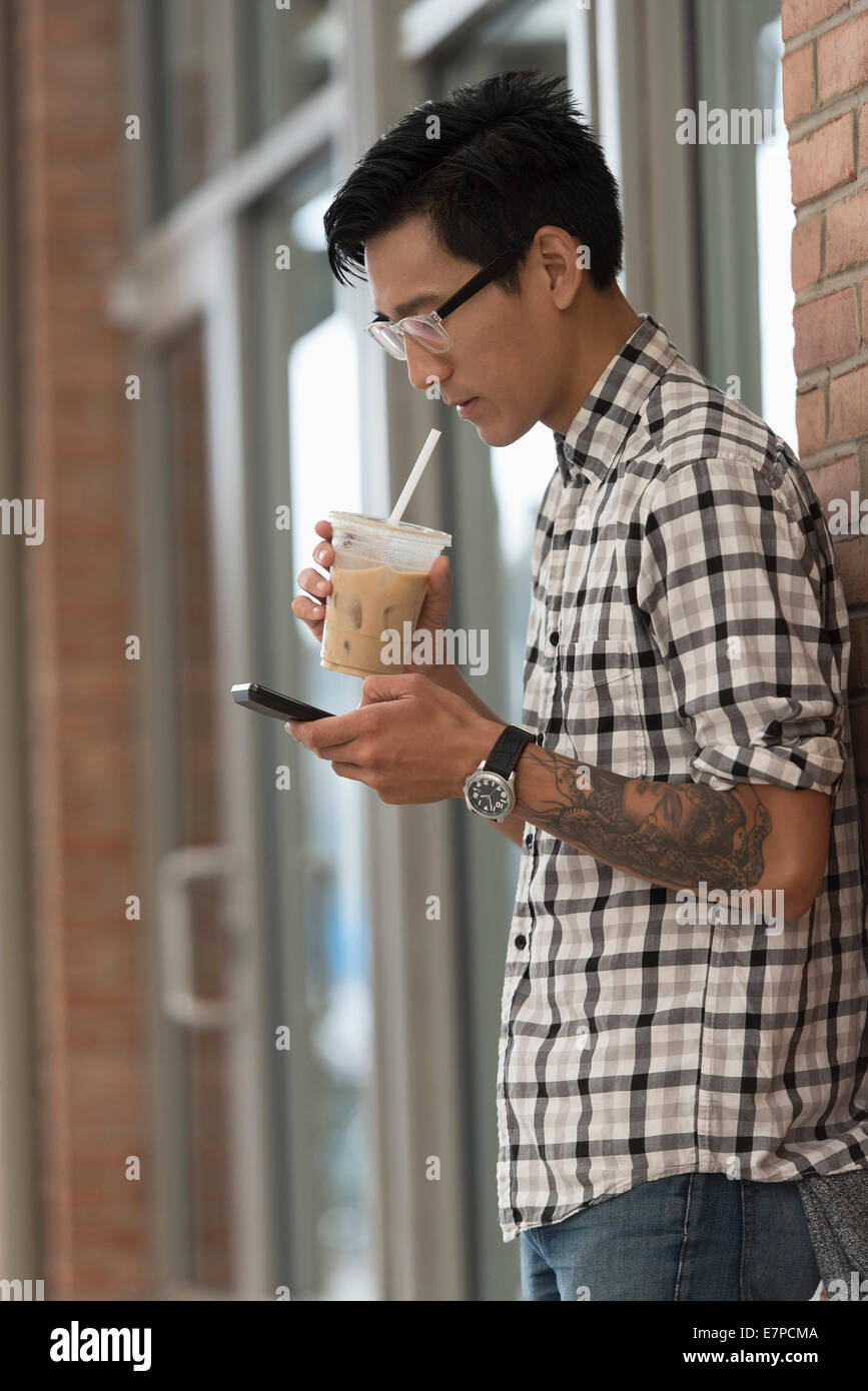 Uomo a camminare sul marciapiede con caffè ghiacciato e il telefono cellulare Foto Stock