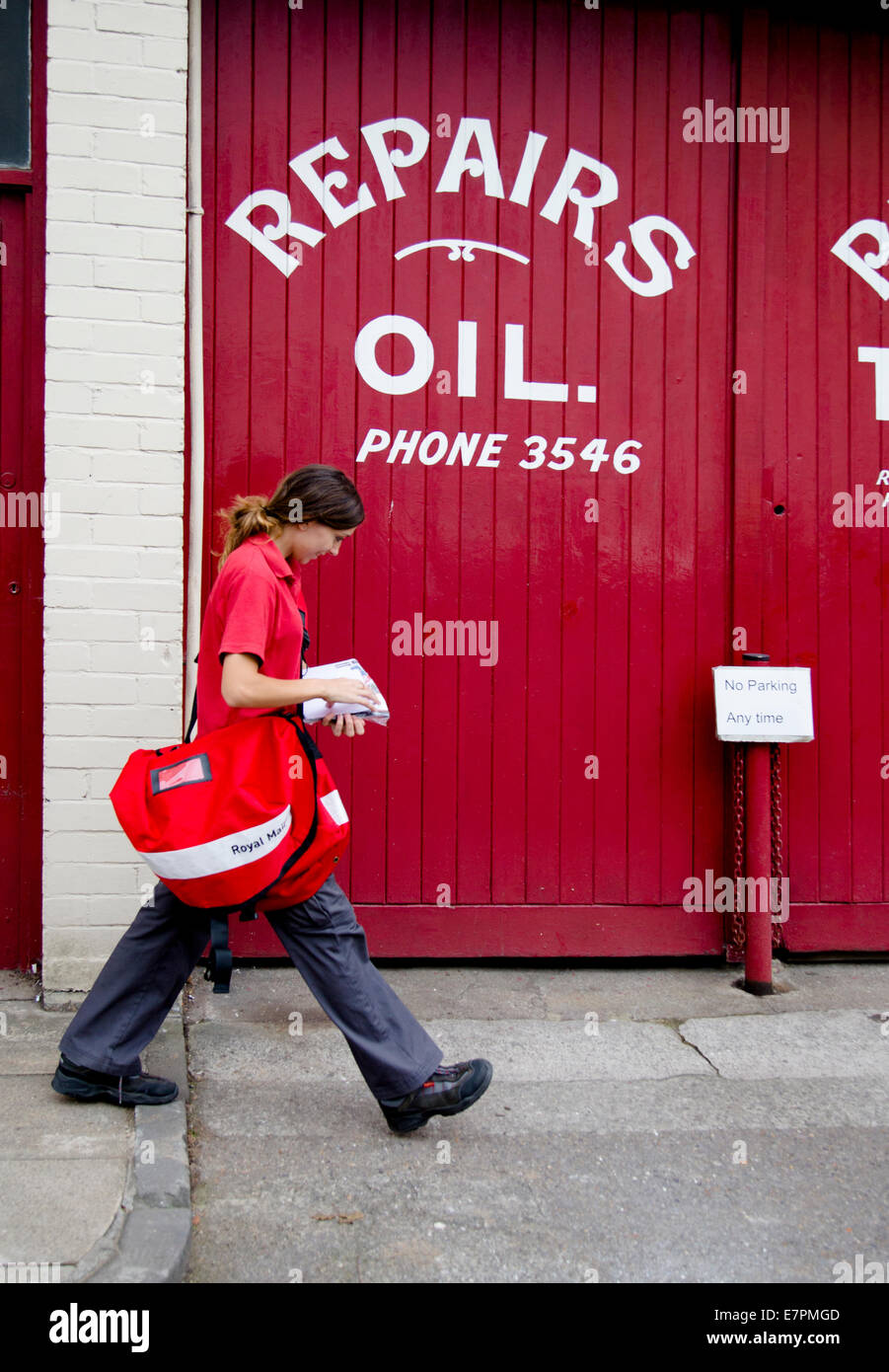 Post woman in red camminando passato red porte di garage in Clifton Bristol REGNO UNITO Foto Stock