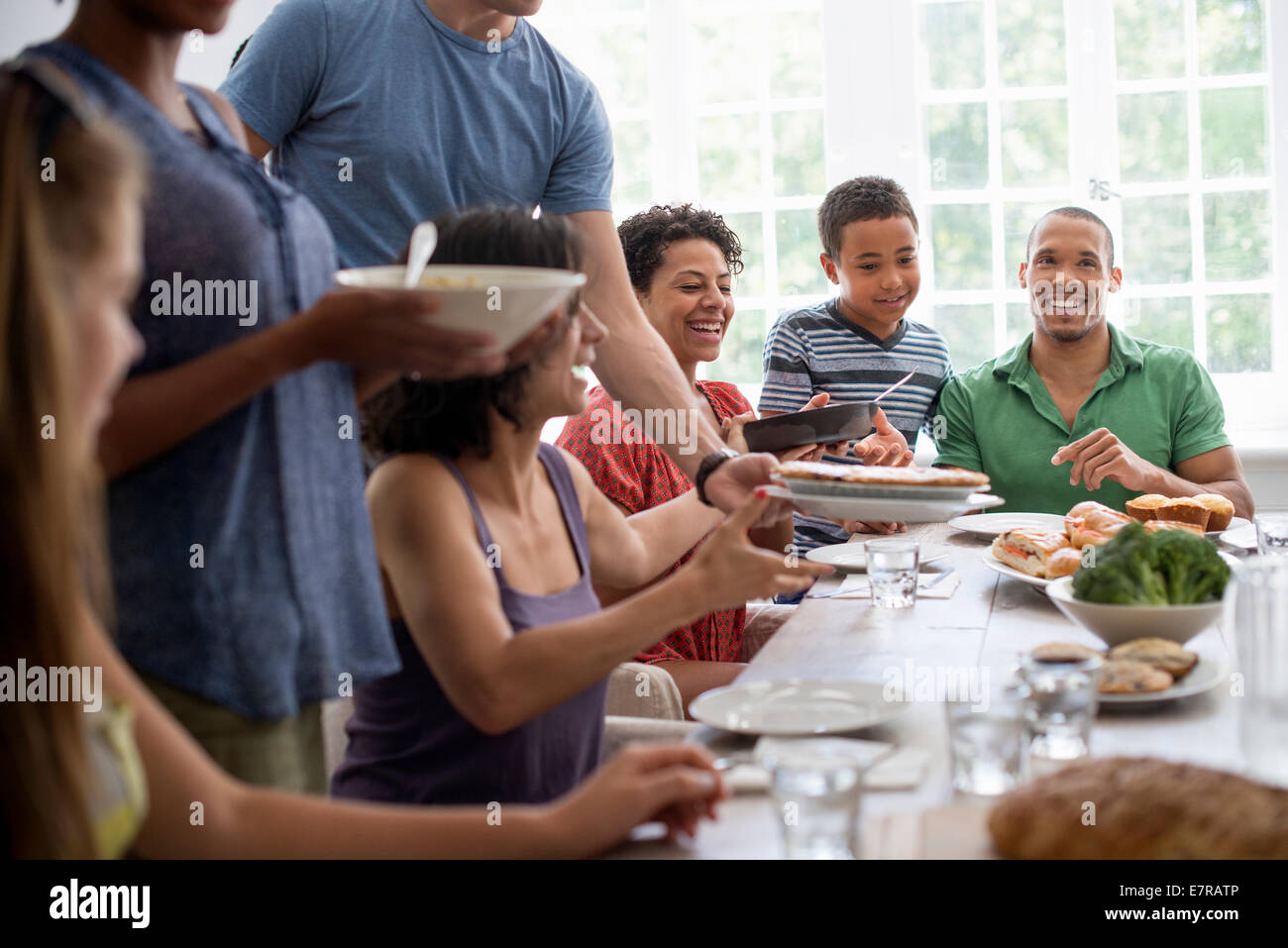 Una riunione di famiglia, uomini, donne e bambini intorno a un tavolo da pranzo la condivisione di un pasto. Foto Stock