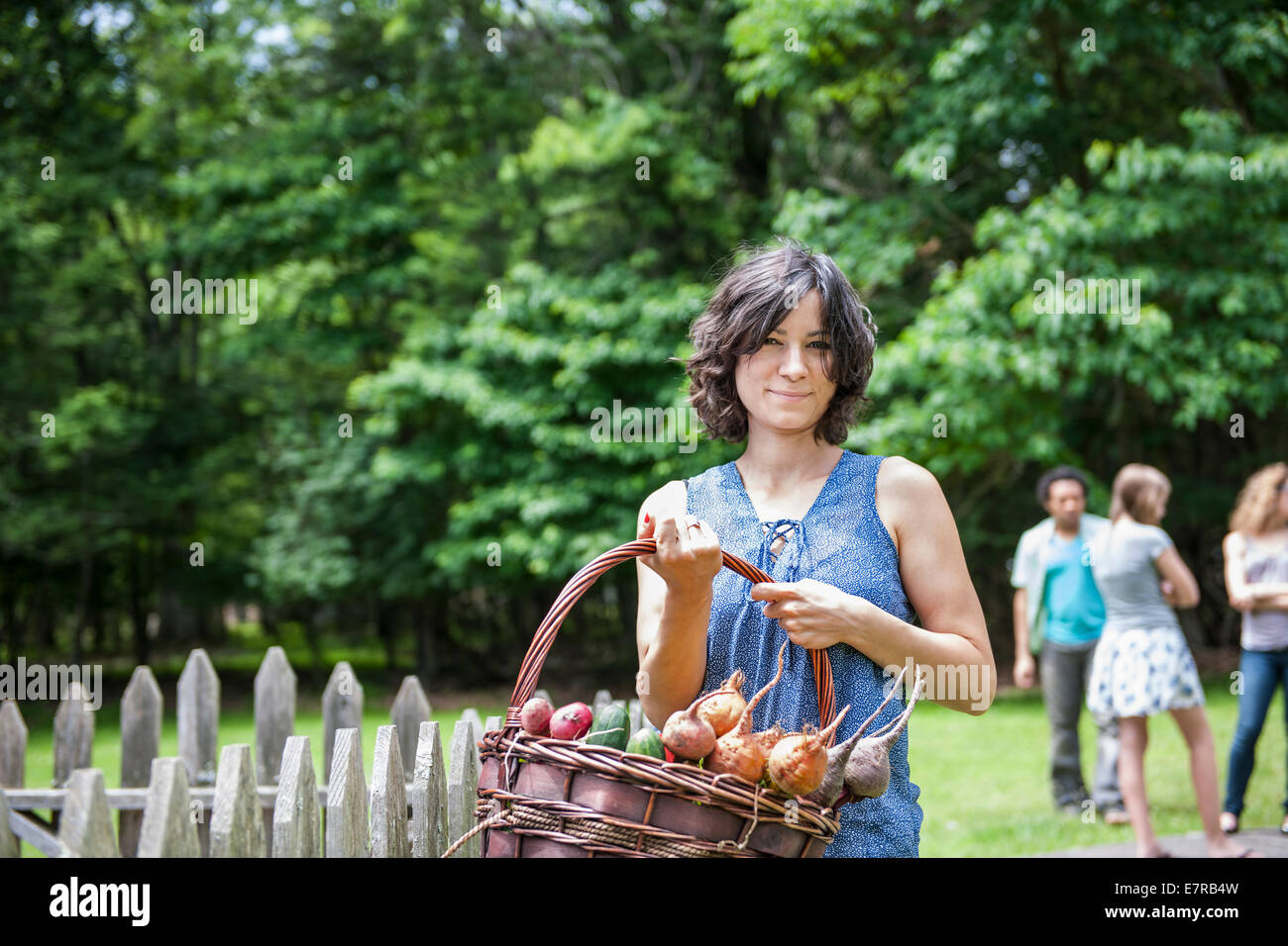 Donna in piedi in un giardino tenendo un cesto di verdure. Foto Stock
