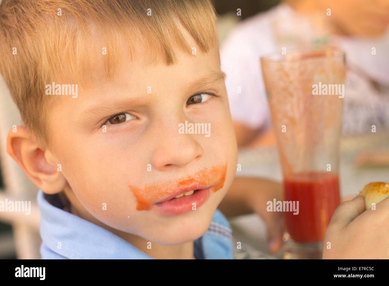 Funny piccolo ragazzo di bere il succo di pomodoro in cafe. Baffi di pomodoro Foto Stock