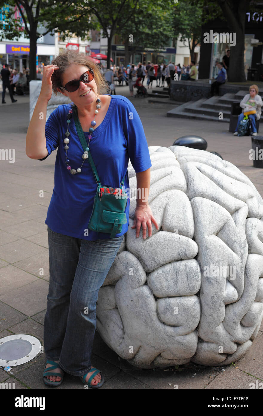 Una donna graffi la sua testa accanto a un cervello di marmo scultura di Anne e Patrick Poirier a Haymarket a Norwich, Norfolk. Foto Stock