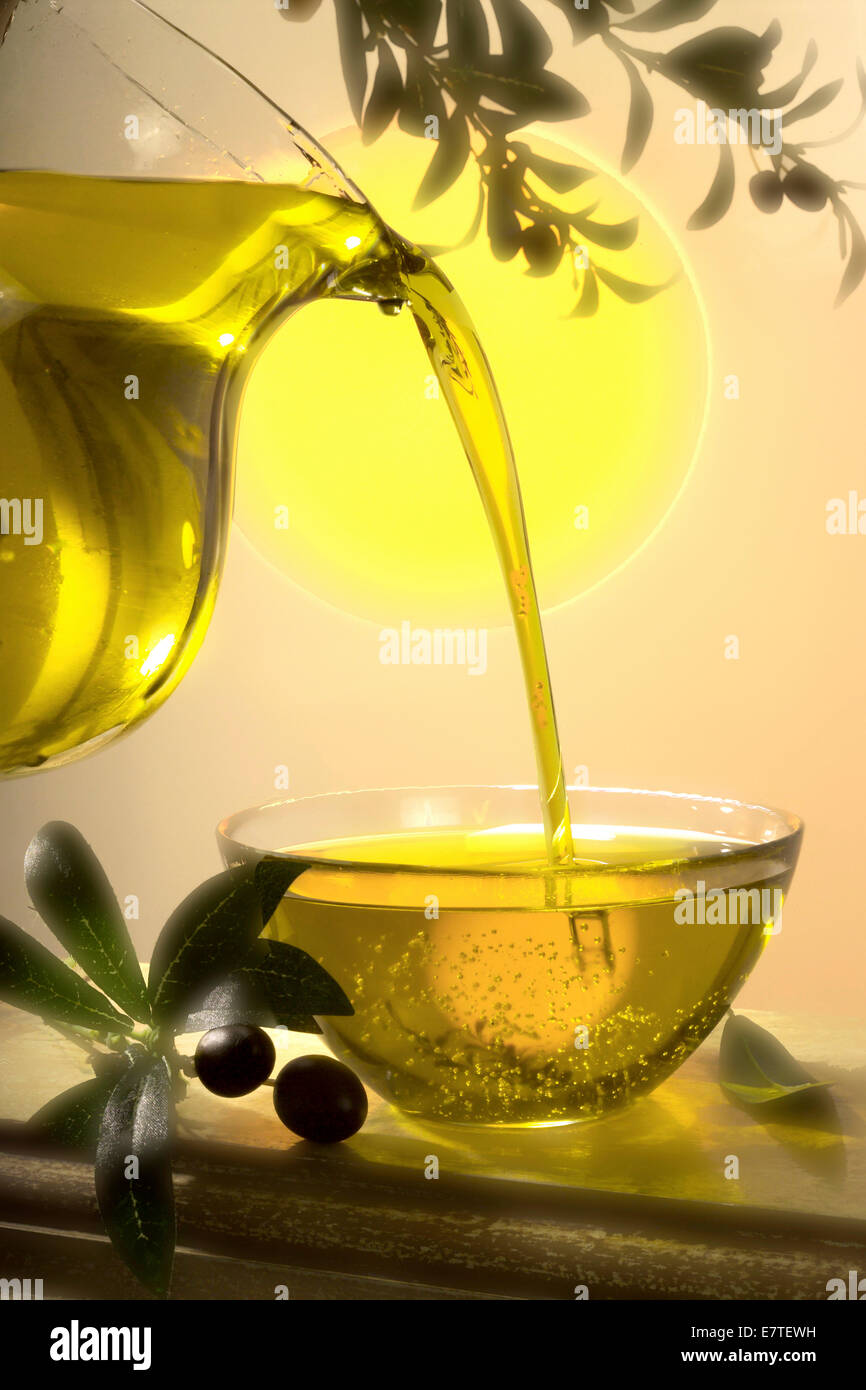 Olio d'oliva che fluisce da una caraffa di vetro in una ciotola di vetro Foto Stock