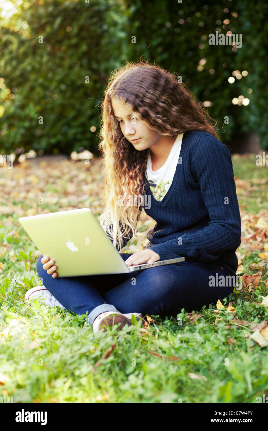 Adolescente ragazza studente con il computer portatile all'aperto nel giardino con foglie cadute. Autunno Foto Stock