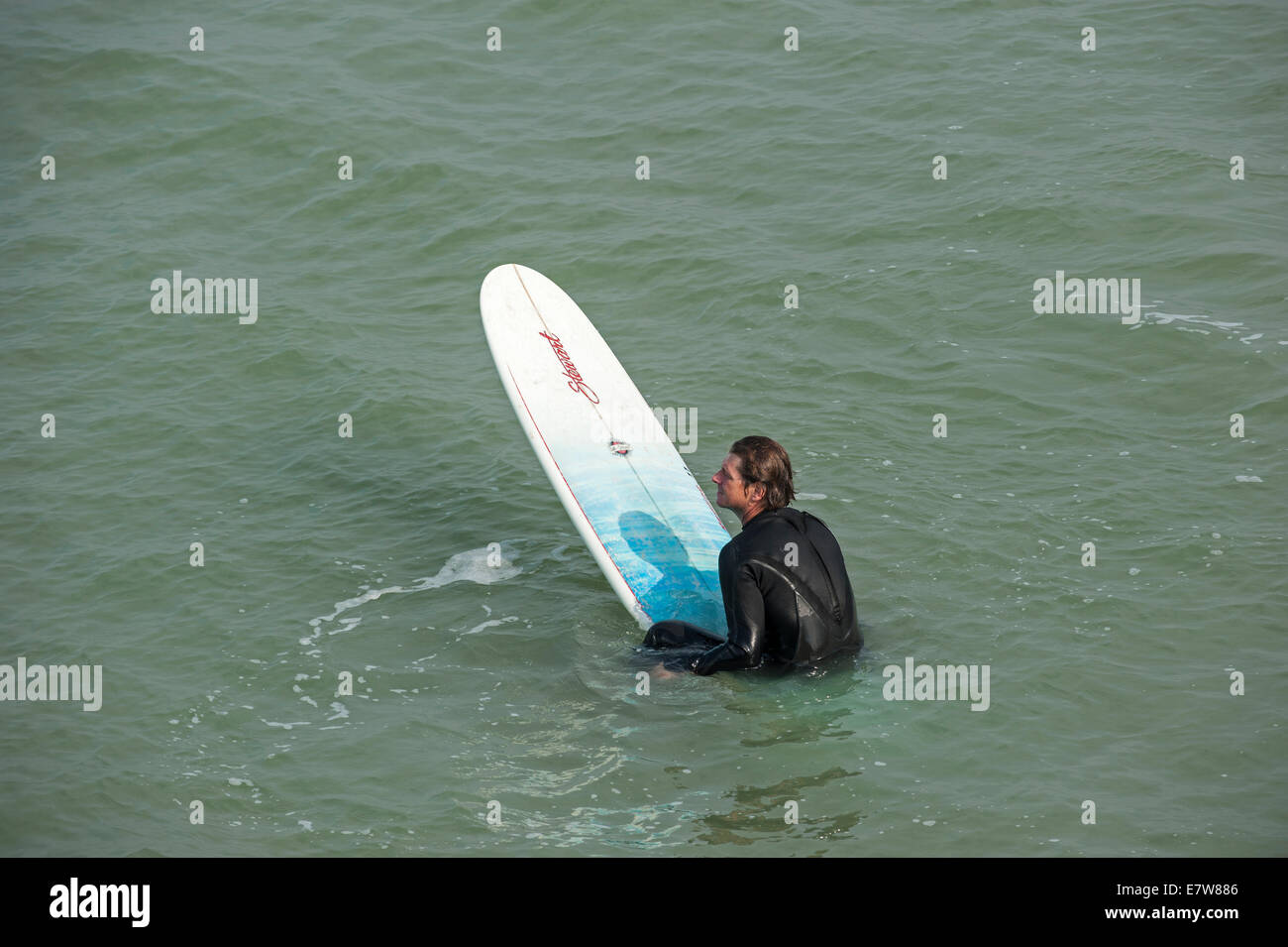 Surfer in wetsuit seduto su una tavola da surf, in attesa di una grande onda / frantumatore per navigare lungo la costa del Mare del Nord Foto Stock