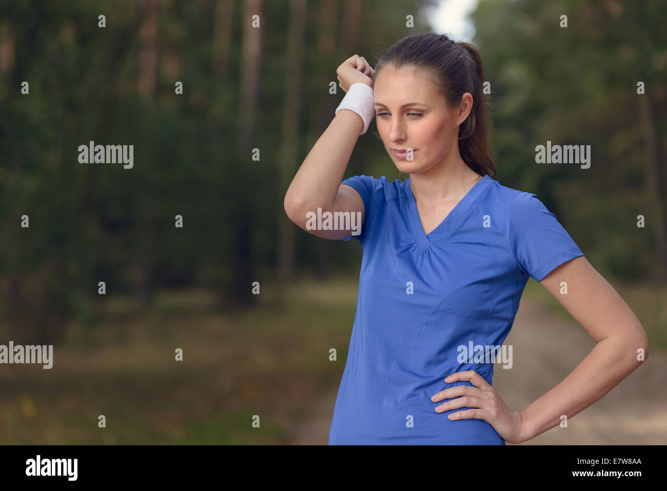 Donna atleta tergi sudore dalla sua fronte sul suo cinturino da polso come si ferma durante la sua formazione esercizi su una pista forestale Foto Stock