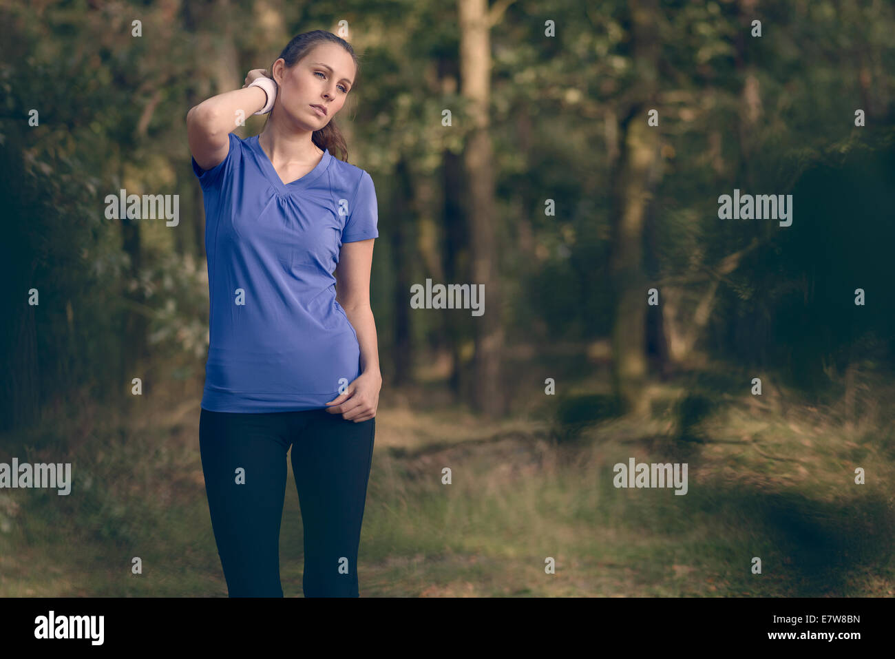 Donna atleta tergi sudore dalla sua fronte sul suo cinturino da polso come si ferma durante la sua formazione esercizi su una pista forestale Foto Stock