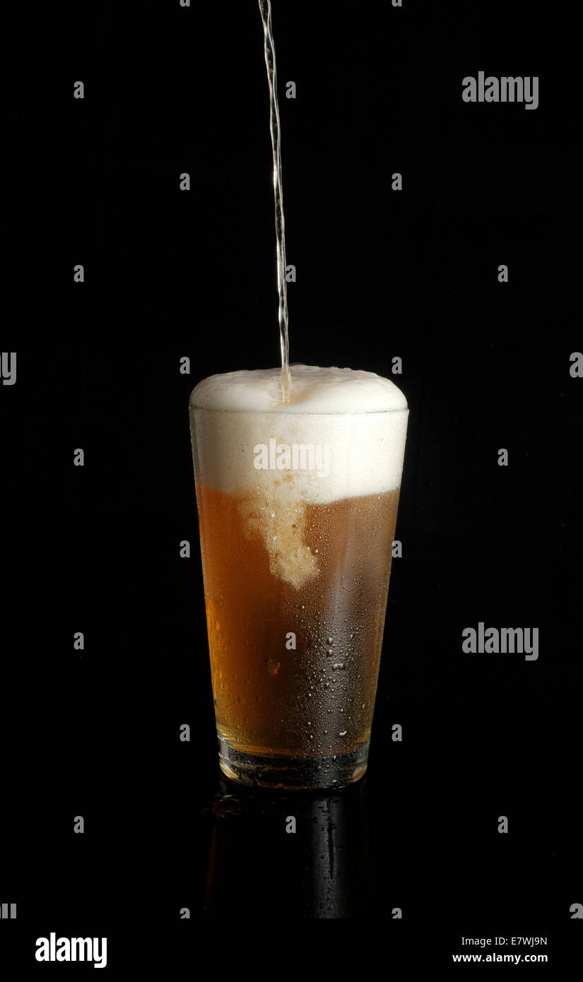 La birra non etichettata viene versata in una pinta di vetro su sfondo nero Foto Stock