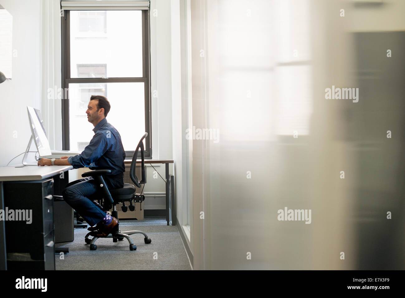 Vita in ufficio. Un uomo in abbigliamento casual seduti ad una scrivania guardando lo schermo di un computer. Foto Stock