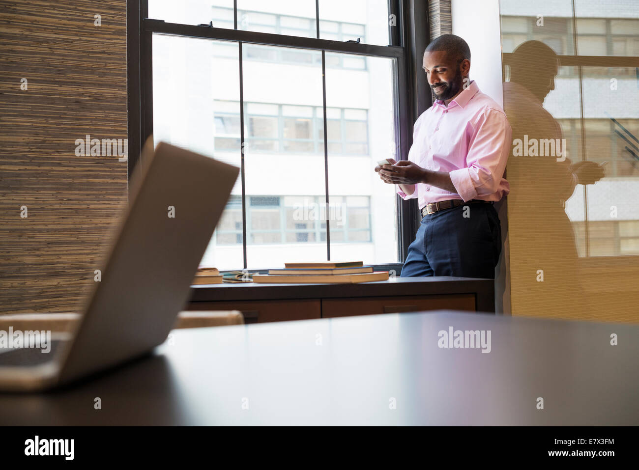Vita in ufficio. Un uomo in piedi da una finestra in un ufficio controllo il suo smart phone. Foto Stock