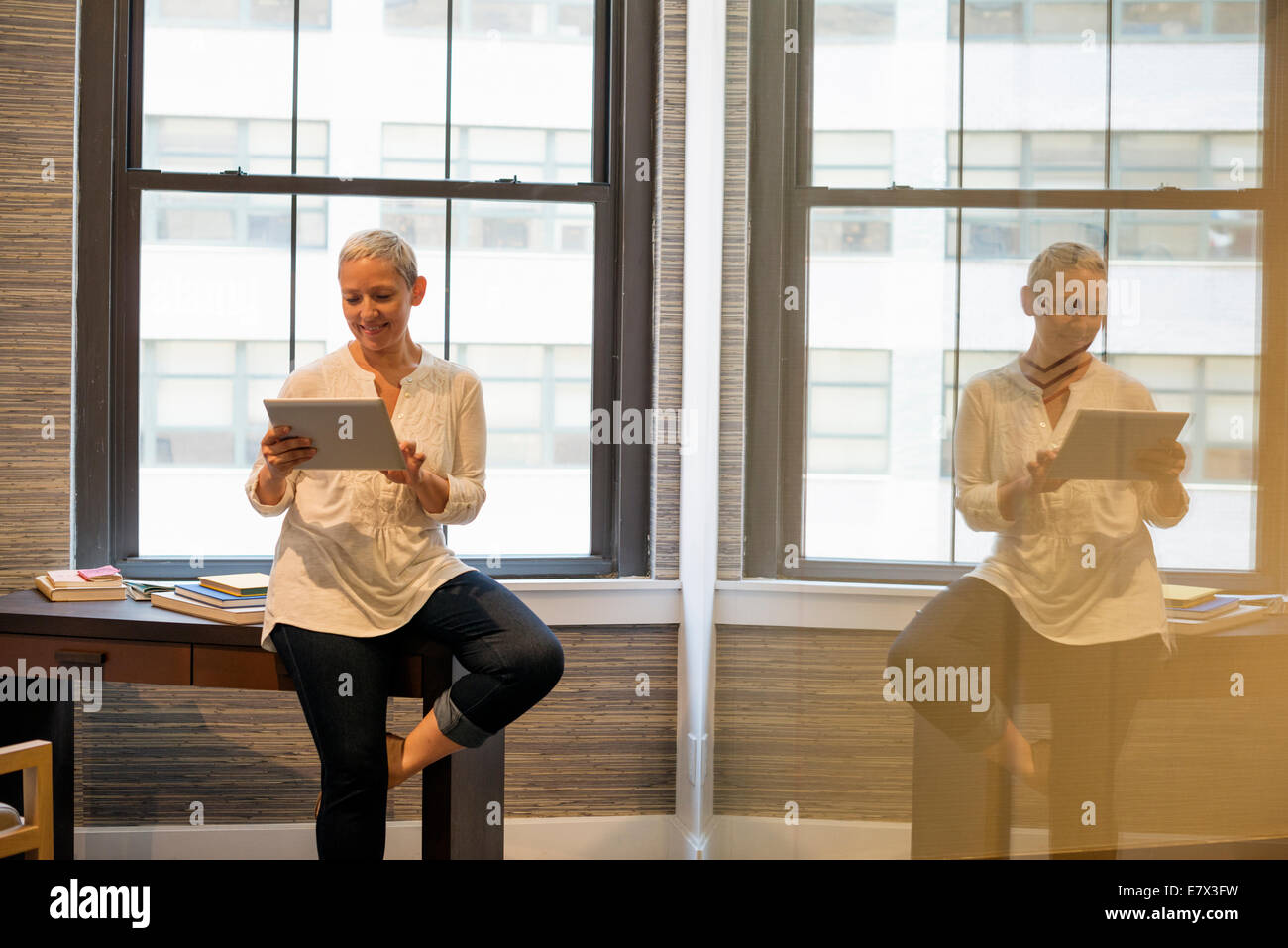 Vita in Ufficio.Una donna seduta sul bordo della sua scrivania utilizzando una tavoletta digitale. Foto Stock