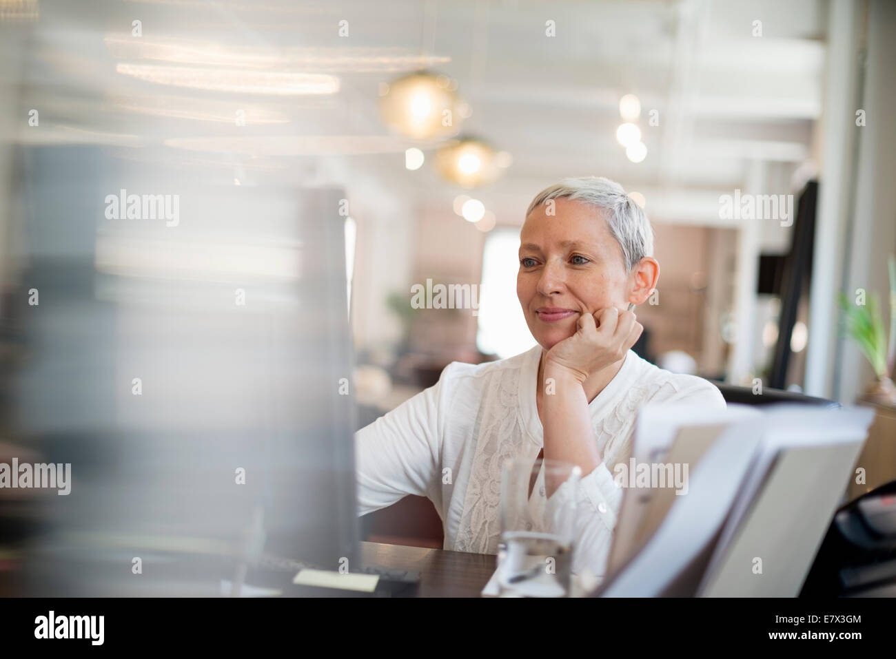 Vita in ufficio. Una donna con il suo mento appoggiato sulla sua mano utilizzando un computer. Foto Stock