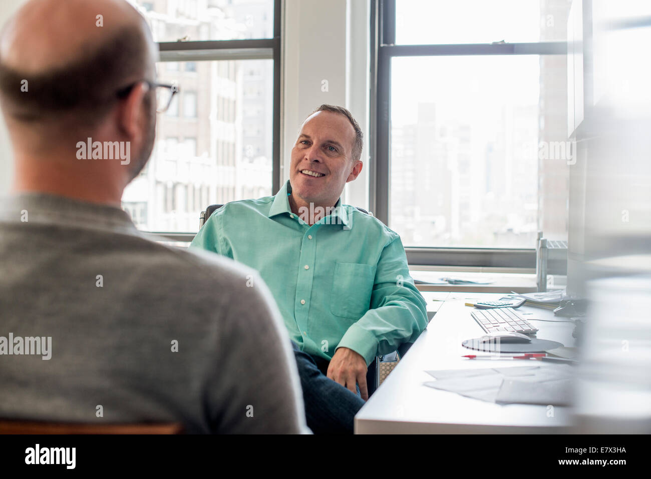 Due uomini seduti in un luminoso e arioso ambiente ufficio, parlando. Foto Stock