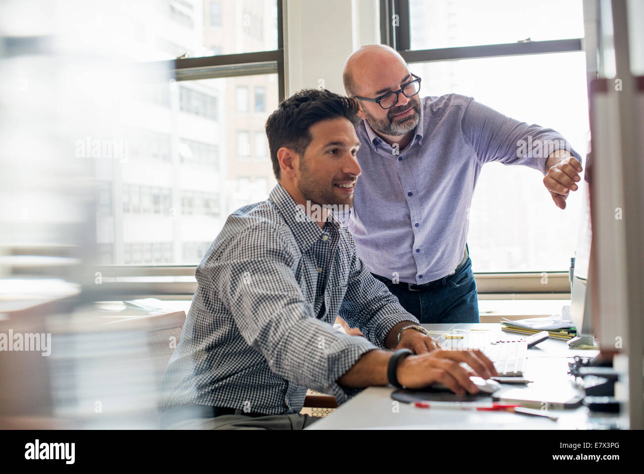 Vita in ufficio. Due uomini in un ufficio, utilizzando lo schermo di un computer. Foto Stock