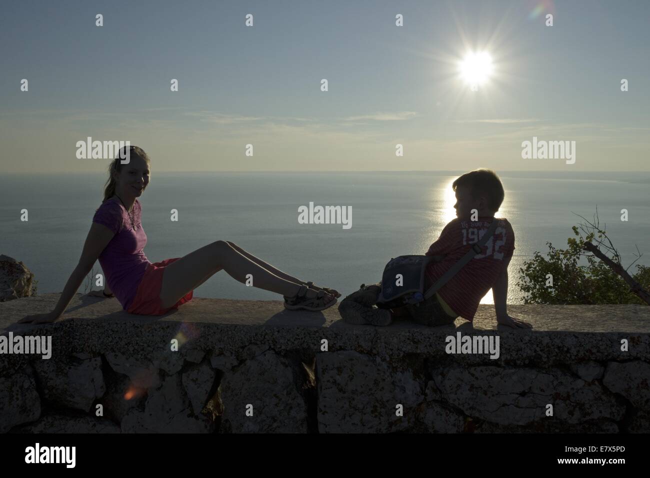 Ragazzo e una ragazza seduta su una parete a guardare il tramonto, Lubenice, Isola di Cherso, golfo di Kvarner, Croazia Foto Stock