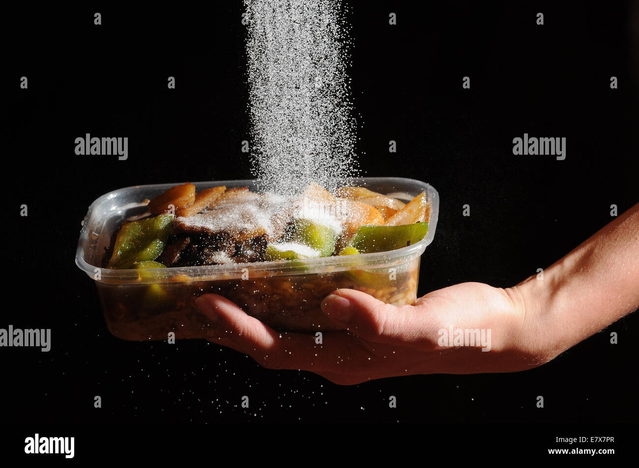 Cibo da asporto con sale che viene versato su dal di sopra. Alti livelli di sale nel cibo spazzatura cause di alta pressione sanguigna e la malattia di cuore Foto Stock