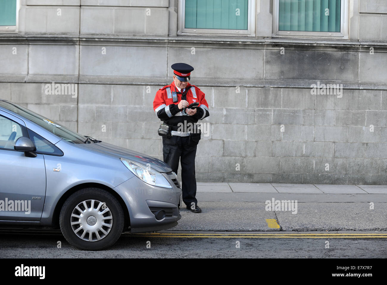 Un vigile (civile esecuzione officer) di pattuglia emettere i biglietti per il parcheggio per le auto parcheggiate in sosta a Cardiff, nel Galles. Foto Stock