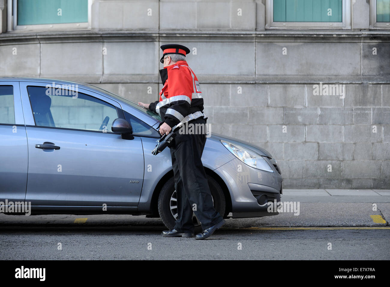Un vigile (civile esecuzione officer) di pattuglia emettere i biglietti per il parcheggio per le auto parcheggiate in sosta a Cardiff, nel Galles. Foto Stock