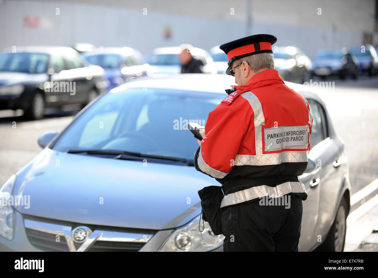 Un vigile (civile esecuzione officer) di pattuglia emettere i biglietti per il parcheggio per le auto parcheggiate in sosta a Cardiff, nel Galles. Foto Stock