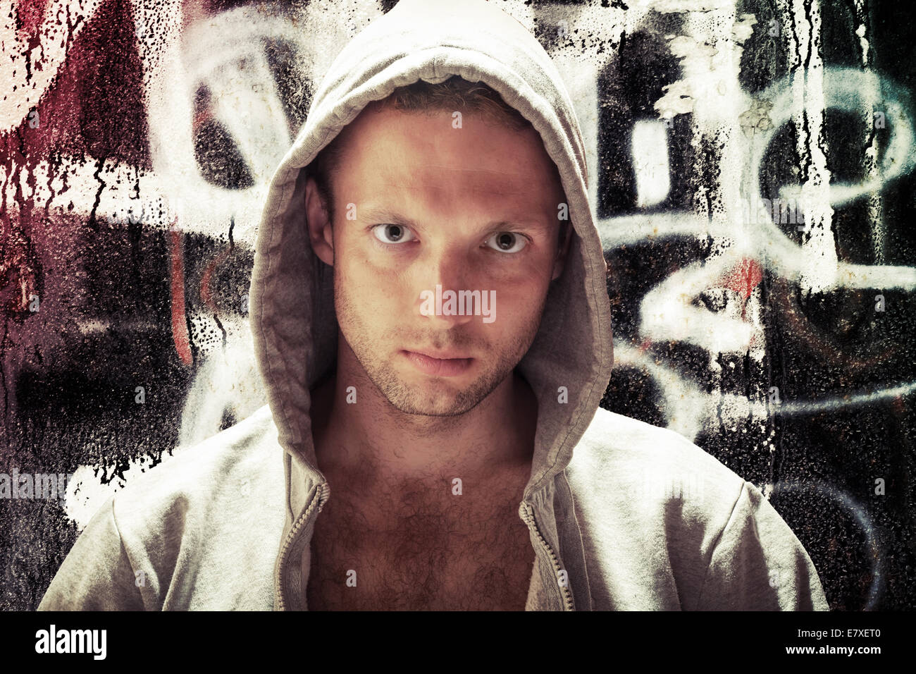 Giovane uomo caucasico nel cofano, artista di strada ritratto con una schifezza muro di graffiti su sfondo, effetto tonico Foto Stock