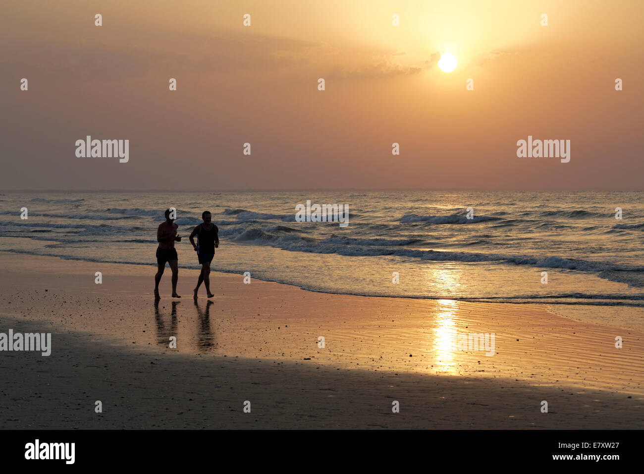 Due uomini jogging sulla spiaggia al tramonto, silhouette, Al-Batinah provincia, Oman, Penisola arabica Foto Stock