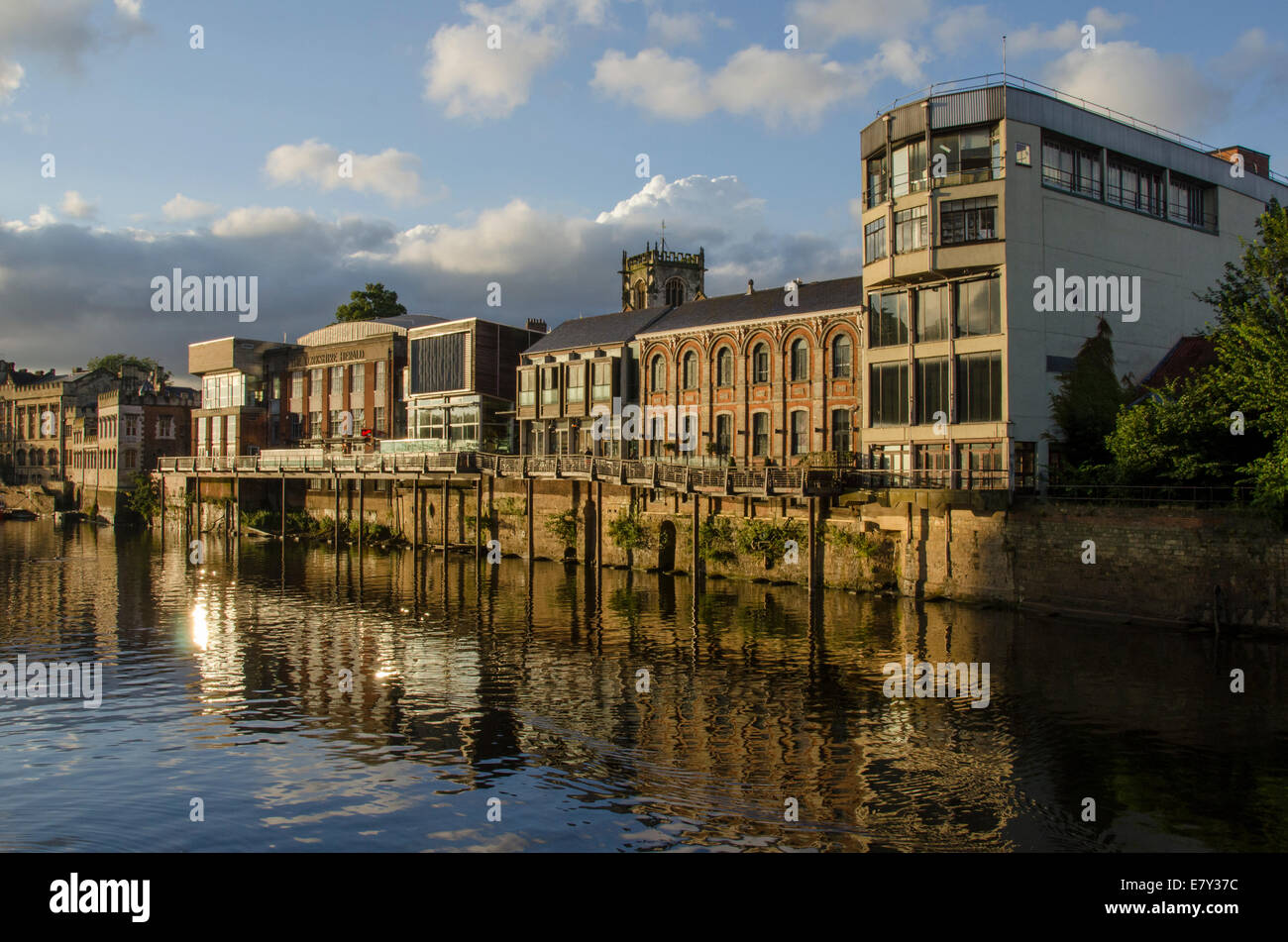 Scenic riverside edifici con lunga passerella balcone, illuminata da una serata estiva sun, che si riflette nel fiume Ouse - York, North Yorkshire, Inghilterra, Regno Unito. Foto Stock
