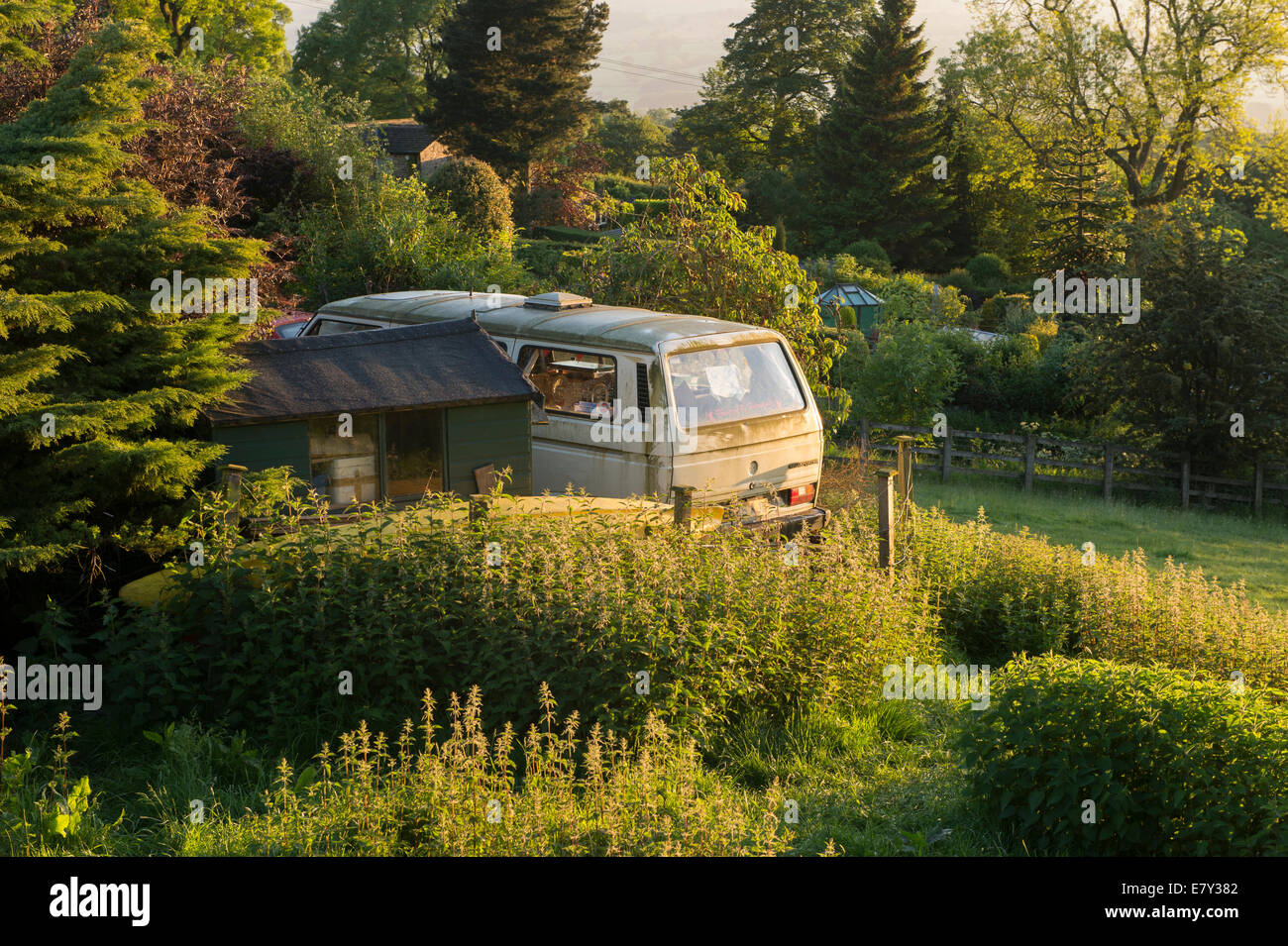 Vecchio e sporco, trascurato, parcheggiato VW Camper Van sembra fuori luogo nella splendida e soleggiata e ben curato giardino - West Yorkshire, Inghilterra, Regno Unito. Foto Stock