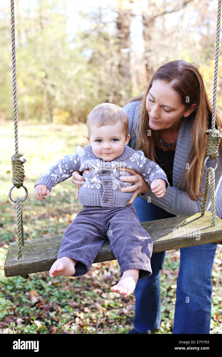 Madre e figlio (12-23 mesi) giocando su swing in posizione di parcheggio Foto Stock