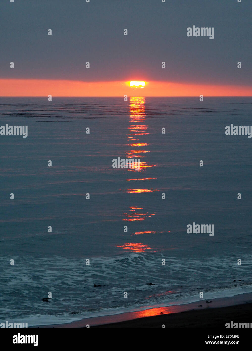 Il sole che tramonta inizia ad apparire da dietro lo strato di nuvole pesante dell'Oceano Pacifico Foto Stock