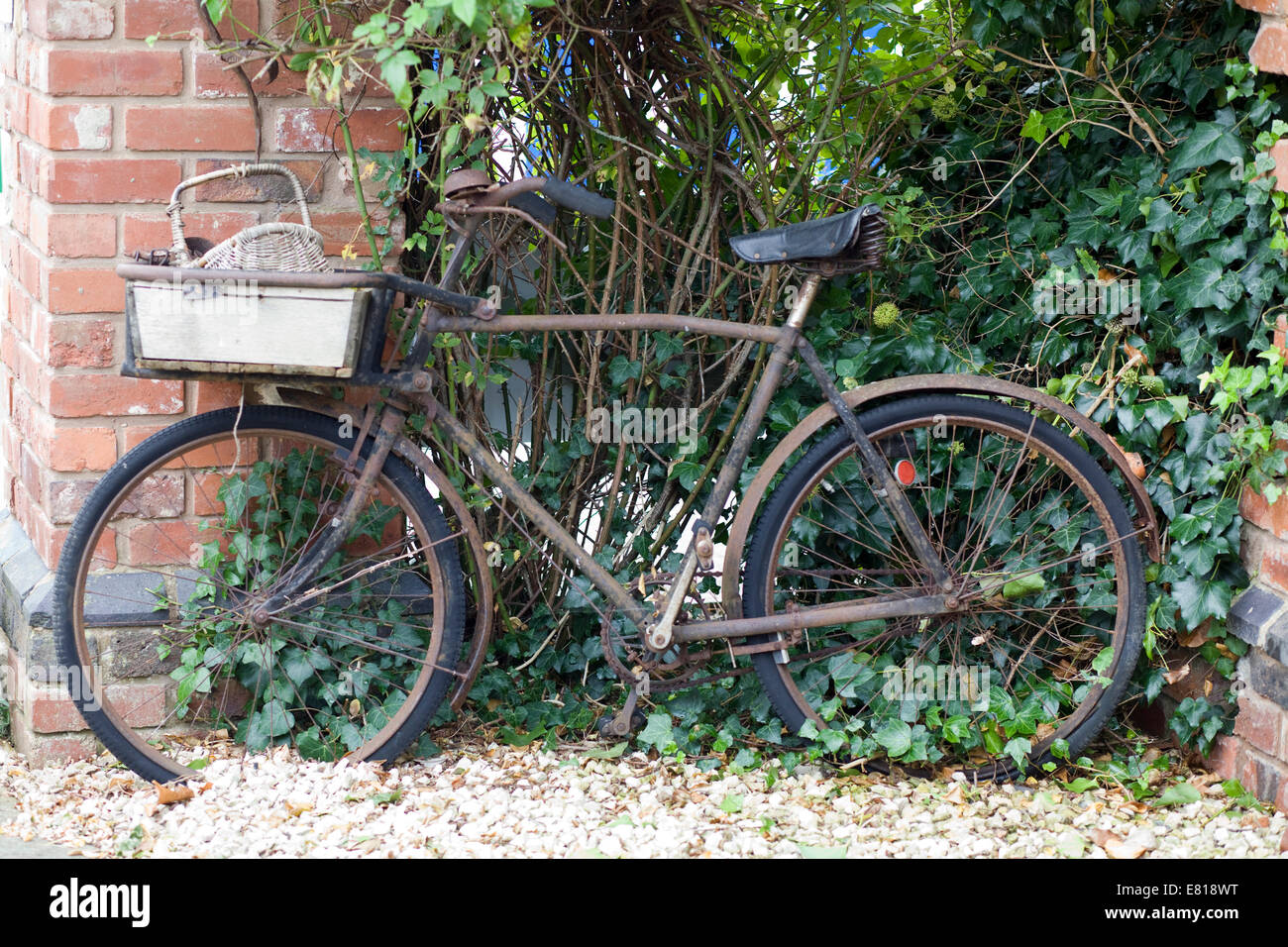 Rusty vintage bicicletta appoggiata contro un rosso muro di mattoni Foto Stock