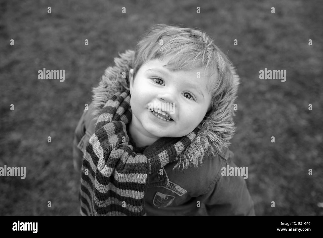 Due anni di vecchio ragazzo che sorride alla telecamera mentre avvolto a caldo per inverno nel suo cappotto e sciarpa Foto Stock