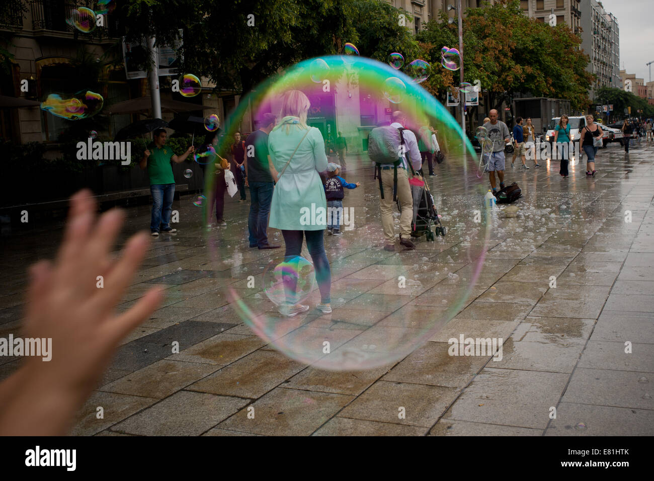 Una mano cercando per far scoppiare una bolla di sapone che passa sopra la cattedrale di Barcellona square. Foto Stock